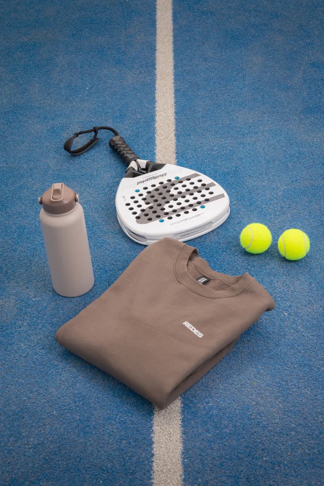 Raquette, gourde et textile REDES sur un court